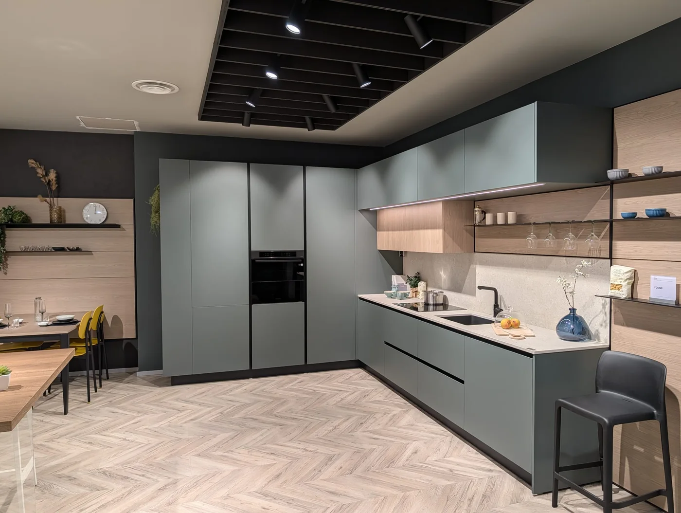 Cucina angolare verde con pensili e dettagli in legno nello showroom di Veduggio
