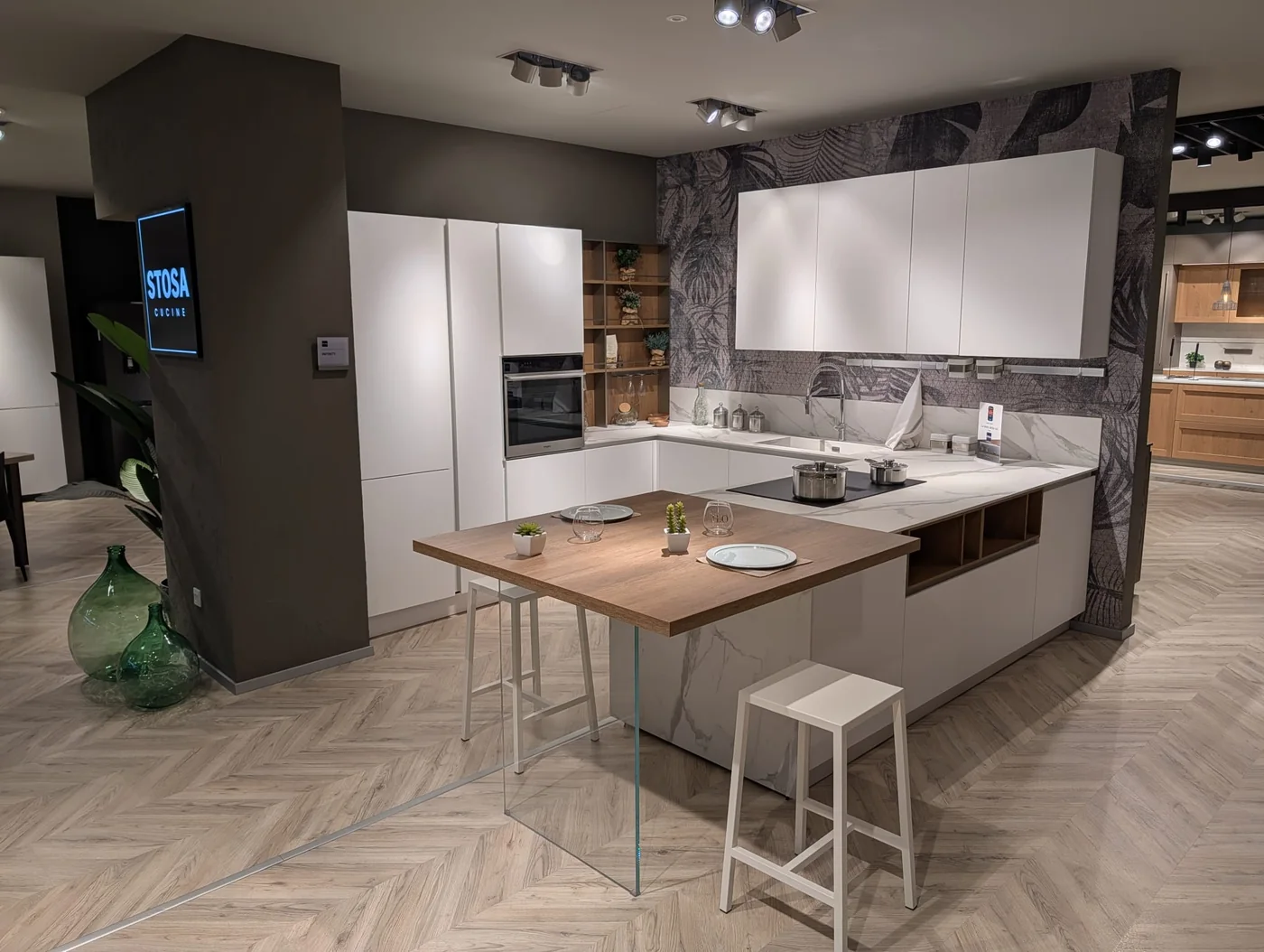 Cucina bianca con penisola e piano snack in legno nello showroom di Veduggio