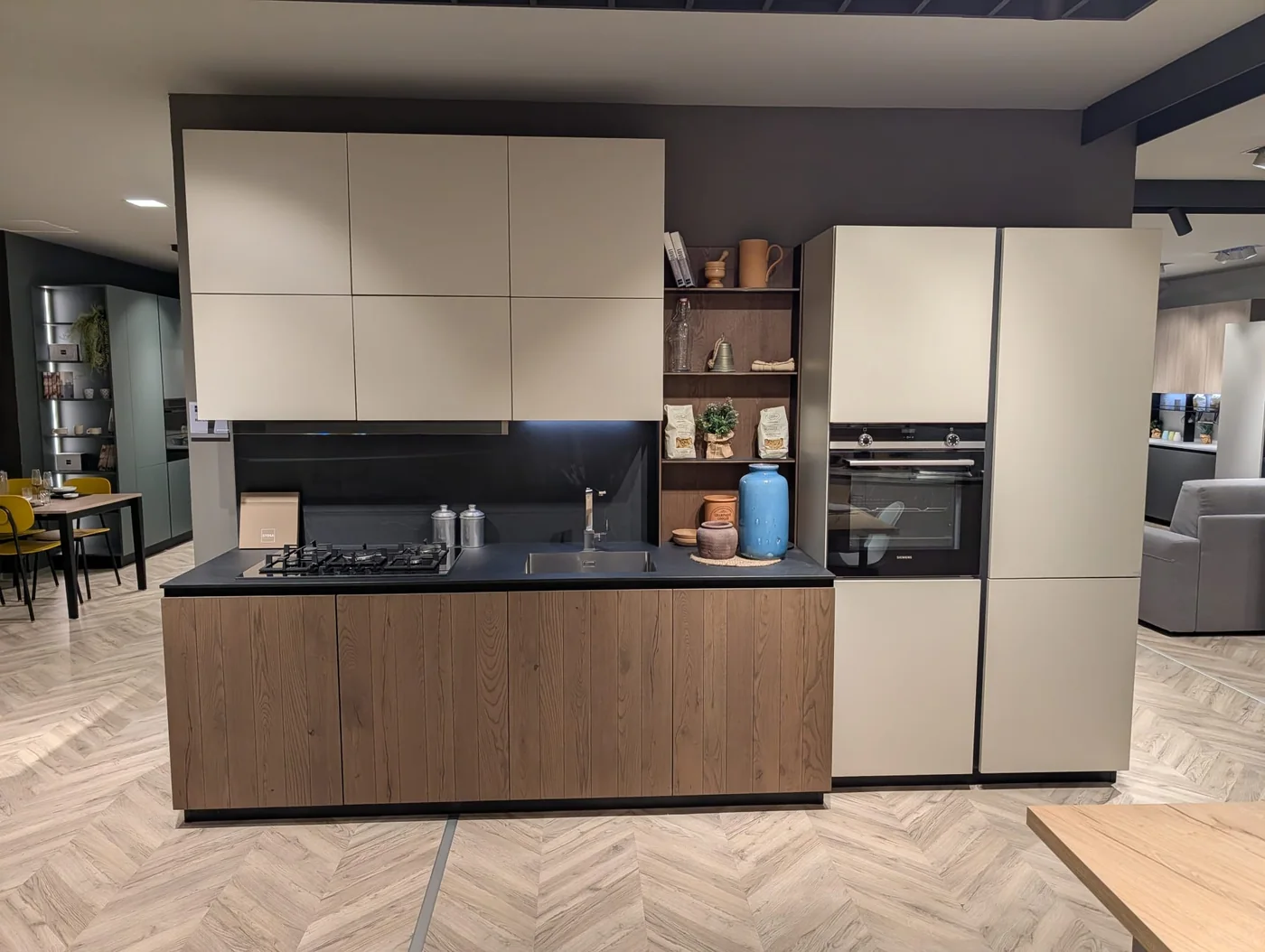 Cucina con basi in legno, pensili chiari e top nero nello showroom di Veduggio